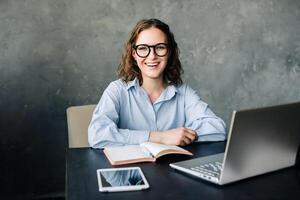 Happy young woman teaching online from her desk with a laptop. Ideal for showcasing remote education, virtual classes, and modern teaching methods in a professional home setting photo