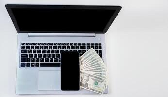 Top view of laptop with cell phone and dollar bills. Cell phone on laptop keyboard and dollar bills. Mobile phone on top of dollar bills on laptop keyboard photo