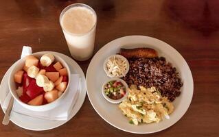 Gallo pinto breakfast served on the table with a fruit salad, Traditional gallopinto dish with fried eggs and a bowl of fruit salad on the table. Traditional gallo pinto served at the table photo