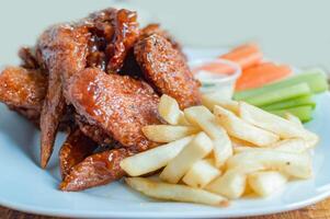 Plate of barbecue wings and fries with ranch sauce, Close up of plate of hot wings and fries served on the table. National typical food concept photo