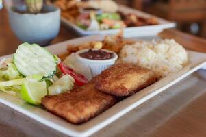 Breaded chicken with salad on wooden table with COPY SPACE, Close up of chicken fillet with salad, rice and beans photo