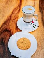 Close up of cookie and cappuccino on wooden table. Top view glass of hot cappuccino with cookie on wooden background photo