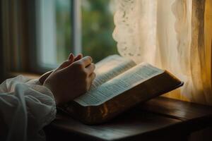 woman's hands folded in prayer on the background of the bible, close up photo