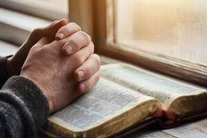 Men's hands folded in prayer on the background of the Bible, close up photo
