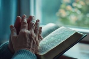 woman's hands folded in prayer on the background of the bible, close up photo
