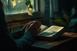 woman's hands folded in prayer on the background of the bible, close up photo
