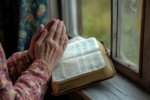 woman's hands folded in prayer on the background of the bible, close up photo