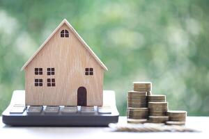 Calculating interest payments, Model house on calculator and stack of coins money on natural green background,Business investment and real estate concept photo