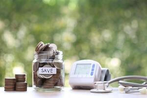 Stack of coins money in glass bottle with stethoscope on green background, Save money for Medical insurance and Health care concept photo