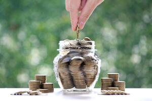 Finance, Woman hand putting a coin into glass bottle on nature green background,Business investment and Save money for prepare in future concept photo