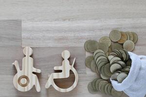 Man on wheelchair and gold coin money in the glass bottle on wooden background,Save money for prepare in future and handicapped person concept photo