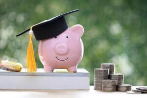 Graduation hat on piggy and stack of coins money on natural green background, Saving money for education concept photo