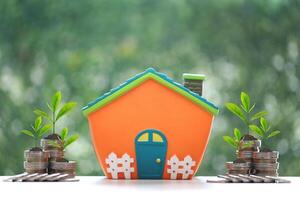 Model house and trees growing on stack of coins money on natural green background,Business investment and real estate concept photo