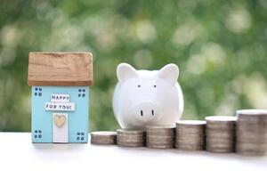 Finance, Model house with piggy bank and stack of coins money on natural green background,Business investment and real estate concept photo