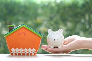 Finance, Model house with piggy bank and stack of coins money on natural green background,Business investment and real estate concept photo