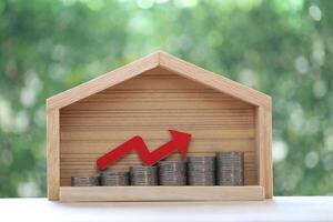 Red arrow graph on stack of coins money in model house on natural green background,Business investment and real estate concept photo