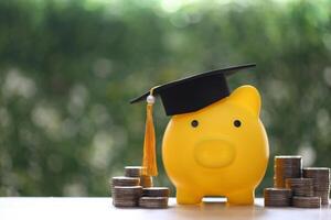 Graduation hat on piggy bank with stack of coins money on nature green background, Saving money for education concept photo