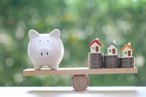 Interest rate up and Banking concept, Model house with piggy bank on wood scale seesaw on natural green background photo