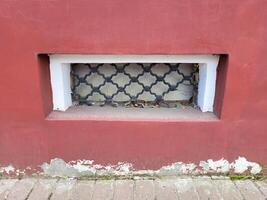 There is a small rectangular window with a wrought iron grille on the red facade of the house photo