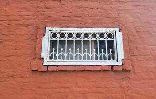 On the red brick facade there is a small rectangular window with a white wrought-iron grille photo