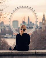 Person sitting on a ledge overlooking the London Eye at sunset photo