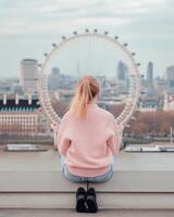 Person sitting on a ledge overlooking the London Eye at sunset photo