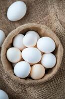 Fresh white eggs in a rustic bowl on a textured burlap cloth photo