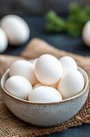 Fresh white eggs in a rustic bowl on a textured burlap cloth photo