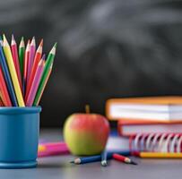 School Supplies With Apple And Colored Pencils On Table Against Blackboard Background photo