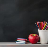 School Supplies With Apple And Colored Pencils On Table Against Blackboard Background photo