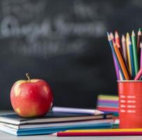 Colorful Pencils and Red Apple on Stacked Books Before Chalkboard photo