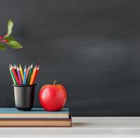 Colorful Pencils and Red Apple on Stacked Books Before Chalkboard photo