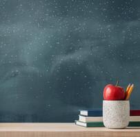 Classroom Desk With Books, Red Apple, And Colorful Pencils On Green Chalkboard Background photo