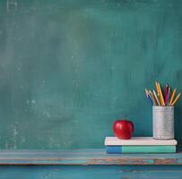 Classroom Desk With Books, Red Apple, And Colorful Pencils On Green Chalkboard Background photo
