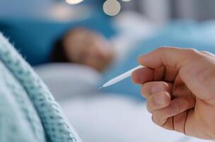 Hand Holding Thermometer Near Person Resting in Bed photo