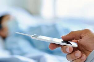 Hand Holding Thermometer Near Person Resting in Bed photo