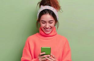 Young Woman Smiling While Texting on Smartphone Against Green Background photo