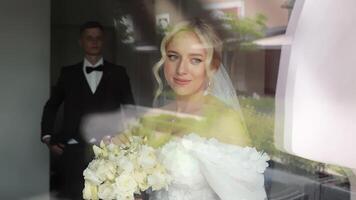 Bride Reflecting Before Wedding Ceremony. A bride stands by a window, holding a bouquet of white roses, with a thoughtful expression on her face. video