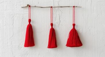 Red Decorative Tassels Hanging on a Branch Against a Rustic White Background photo