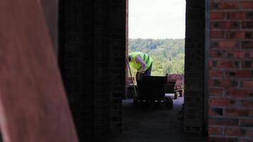 Construction worker bending over at a building site. A construction worker in a high-visibility vest bends over while working on a building site. video
