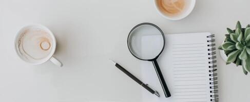 Magnifying Glass on Notepad With Pen and Succulent Plant on White Surface photo