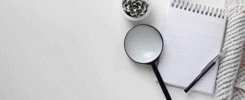 Magnifying Glass on Notepad With Pen and Succulent Plant on White Surface photo