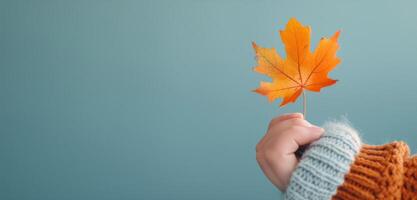 Hand Holding Yellow Maple Leaf Against Blue and Orange Background photo