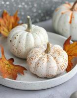 Autumn Decor Featuring White and Orange Pumpkins With Dried Leaves on a Rustic Plate photo