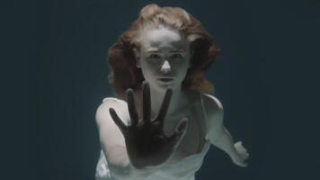 beautiful red-haired girl stopped underwater in front of the camera and froze video