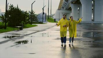 Couple walks around town in those yellow raincoats that are waterproof, and then they realize it's stopped raining and they take them off. video