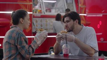 couple est en mangeant une Burger dans de face de une nourriture camion. dans le arrière-plan, vous pouvez voir une client choisir une repas de le menu. lent mouvement video