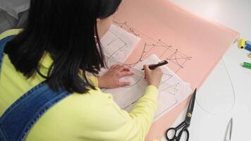 A young haberdasher draws a dotted line on the blueprint in order to subsequently excise any superfluous material. High angle video