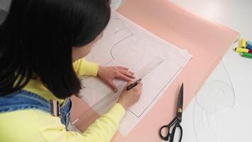 Young craftswoman uses a ruler and marker to draw the outlines of the patterns for the vest. Top view video