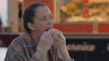 Young woman takes a large bite of a large hamburger, completely absorbed in the experience, and unintentionally gets some of the sauce on her face. Close up. Slow motion video